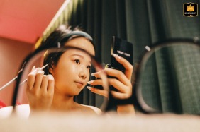 Morning preparations in Kaifeng, Henan, show a bridesmaid seated as she has her makeup applied, highlighting a calm and focused atmosphere before the day's celebrations begin.